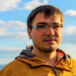 Photo of Lyubomir Pozharliev, standing outside in the sun, wearing glasses and a yellow jacket